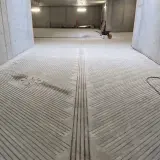 Betonowa pochylnia do garażu podziemnego z antypoślizgowymi nacięciami. Widać studzienkę kanalizacyjną i wózek widłowy w oddali.