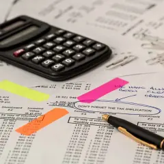 Kalkulator, notatki i dokumenty finansowe. Na jednym z nich widnieje napis "DON'T FORGET THE TAX IMPLICATION", sugerujący rozważania nad **podatkiem rolnym**.