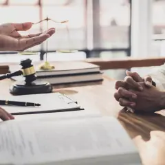 Prawnik omawia z klientem formalności związane z wnioskiem o stwierdzenie nabycia spadku. Na stole leżą dokumenty, młotek sędziowski i waga sprawiedliwości.