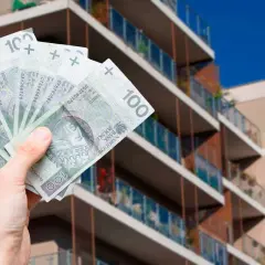 Dłoń trzyma banknoty 100 zł na tle nowoczesnego apartamentowca. Pytanie: jak zapłacić podatek od wynajmu mieszkania?