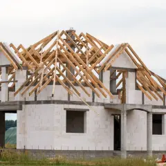 Dom piętrowy w budowie, z widocznym szkieletem dachu. Rozpoczynają się prace nad dachem, co wpływa na koszt budowy domu piętrowego.