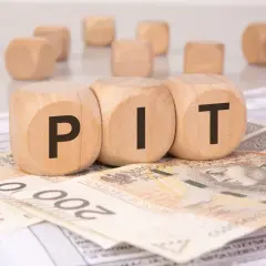 Drewniane kostki z literami "PIT" leżą na banknotach 200 zł i dokumentach podatkowych. To symbol podatku od darowizny.
