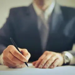 Mężczyzna w garniturze podpisuje dokumenty dotyczące sprzedaży części wspólnej we wspólnocie mieszkaniowej.