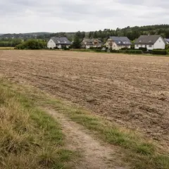 Pole po orce, przygotowane do odrolnienia działki. W tle domy jednorodzinne i las.