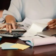 Kobieta liczy na kalkulatorze, przygotowując wniosek o wydanie zaświadczenia w sprawie podatku od spadków i darowizn.