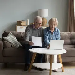 Starsi ludzie przeglądają dokumenty na laptopie, planując zachowek po rodzicach.