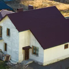 Nowy dom w zabudowie zagrodowej z ciemnobrązowym dachem i jasnymi ścianami, w trakcie budowy.