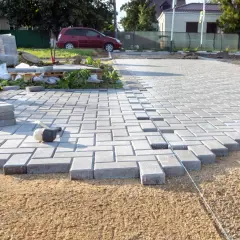 Trwa utwardzenie terenu pod parking. Układanie kostki brukowej, w tle samochód i materiały budowlane.