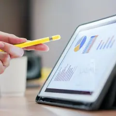 Dłoń z żółtym rysikiem wskazuje na wykresy na tablecie. Analiza danych, być może dotyczących hipoteki odwróconej, w biurze.