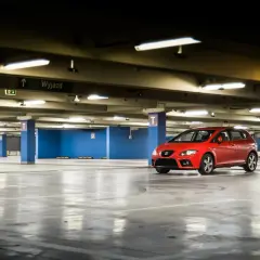 Czerwony samochód na pustym parkingu podziemnym. W tle tablica "Wyjazd". Może to być wizualizacja opłat za garaż we wspólnocie mieszkaniowej.