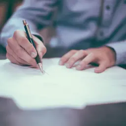 Ręka pisze piórem na dokumencie. To może być wniosek o udostępnienie dokumentów wspólnoty mieszkaniowej wzór.