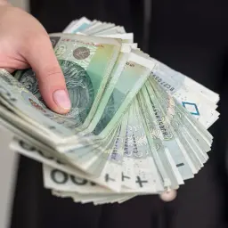 Dłoń trzyma plik banknotów, symbolizujących zwrot kosztów za czynsz od spadkobierców.
