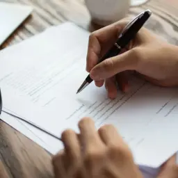 Ręka pisze długopisem na dokumencie, który może być wzorem pełnomocnictwa w sprawie spadkowej. Obok leżą okulary.