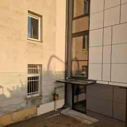 Nowoczesna winda w bloku z wielkiej płyty, z przeszklonym szybem i panelami elewacyjnymi.