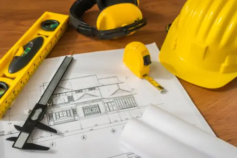Projekt domu, miarka, poziomica, suwmiarka i kask – narzędzia do weryfikacji, czy budynek odebrany ale niezgodny z projektem.