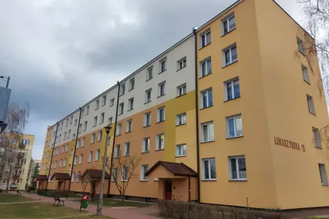 Długi blok mieszkalny przy ul. Łukaszyńskiej 15, pomalowany na żółto i biało. Spółdzielnia mieszkaniowa nie chce naprawić dachu, mimo że przecieka.