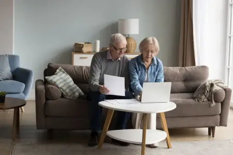 Starsi ludzie przeglądają dokumenty na laptopie, planując zachowek po rodzicach.