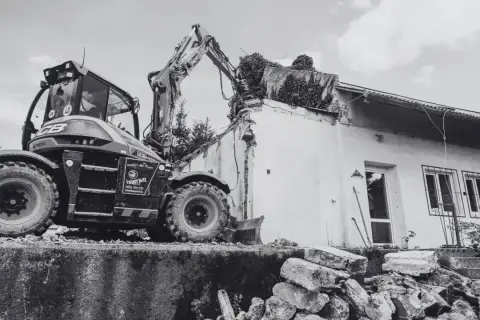 Koparka niszczy budynek. Pamiętaj, ile jest ważne pozwolenie na rozbiórkę, by uniknąć problemów prawnych.