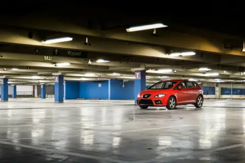 Czerwony samochód na pustym parkingu podziemnym. W tle tablica "Wyjazd". Może to być wizualizacja opłat za garaż we wspólnocie mieszkaniowej.