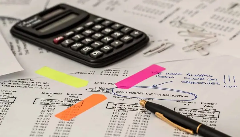 Kalkulator, notatki i dokumenty finansowe. Na jednym z nich widnieje napis "DON'T FORGET THE TAX IMPLICATION", sugerujący rozważania nad **podatkiem rolnym**.