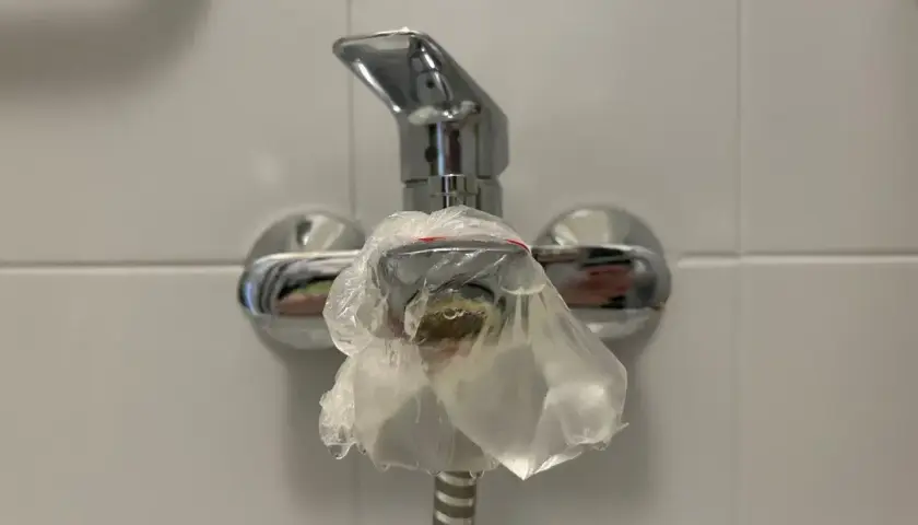 Kran prysznicowy owinięty folią, bo w bloku brak ciepłej wody. Krople zimnej wody spływają po opakowaniu.