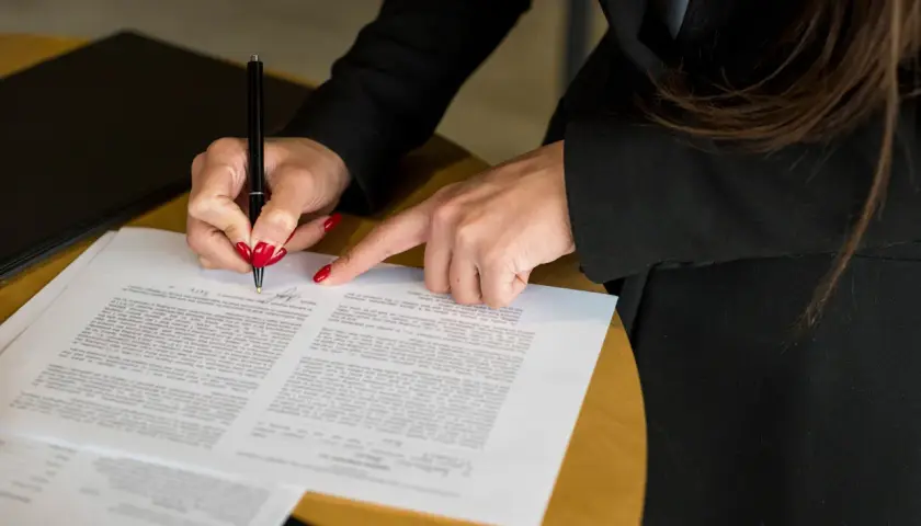Kobieta z czerwonymi paznokciami podpisuje dokument, który może być wpisem do księgi wieczystej.