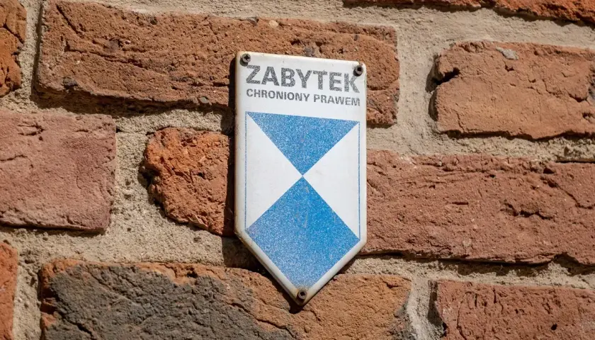 Tabliczka "Zabytek chroniony prawem" na ceglanej ścianie. Może być potrzebna do wypełnienia wzoru wniosku o wykreślenie z gminnej ewidencji zabytków.