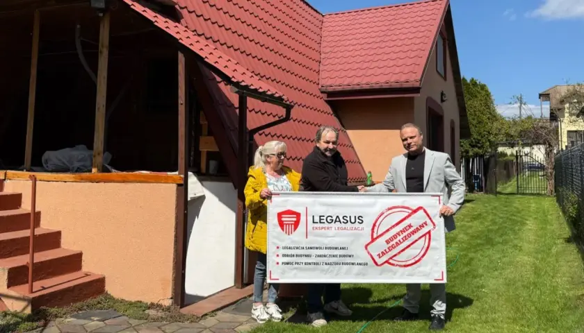 Trzy osoby trzymają baner "BUDYNEK ZALEGALIZOWANY" od Legasus. Wzór zgłoszenia samowoli budowlanej jest widoczny.