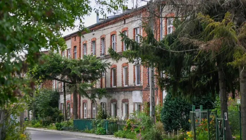 Stary budynek z cegły, zarośnięty zielenią. Właściciele zastanawiają się nad kosztami zarządu nieruchomością wspólną, planując remont.