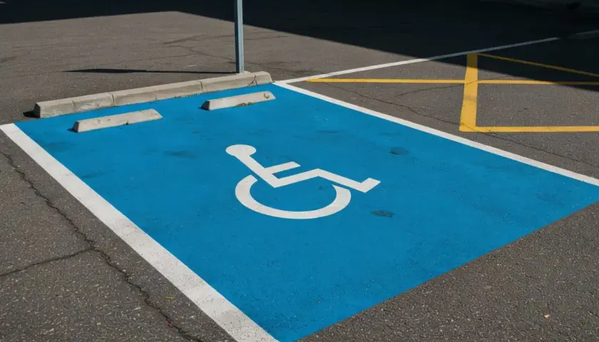 Niebieskie miejsce parkingowe dla niepełnosprawnych, oznaczone symbolem wózka, jest częścią wspólnoty dbającej o dostępność.