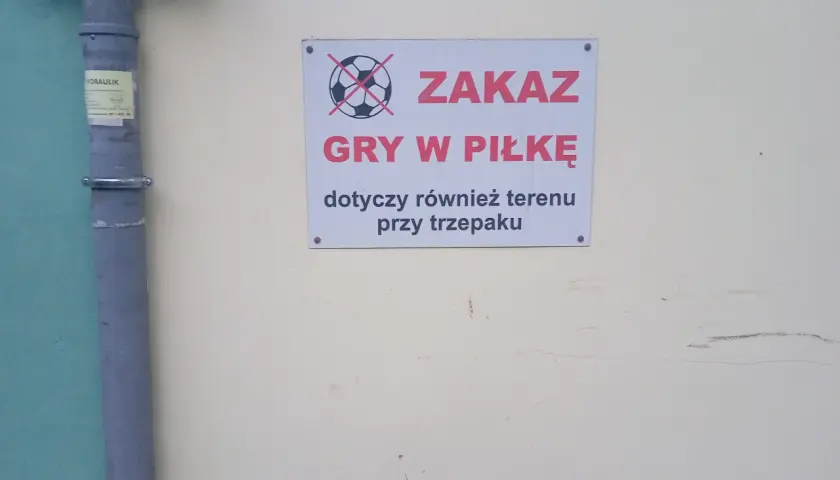 Tabliczka z przekreśloną piłką informuje o zakazie gry w piłkę pod oknami i przy trzepaku.