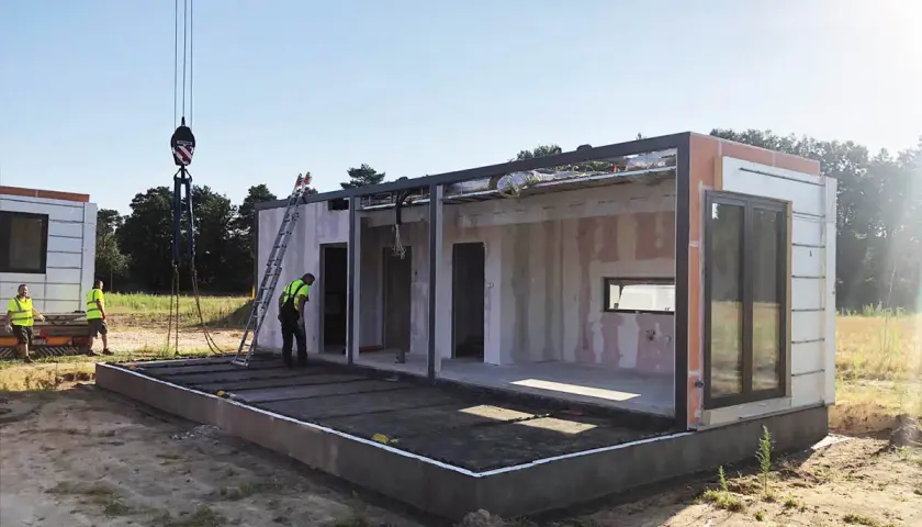 Budowa domu modułowego w toku. Dźwig podnosi element, pracownicy nadzorują montaż. To etap, gdy pozwolenie na budowę i prawo budowlane są kluczowe.