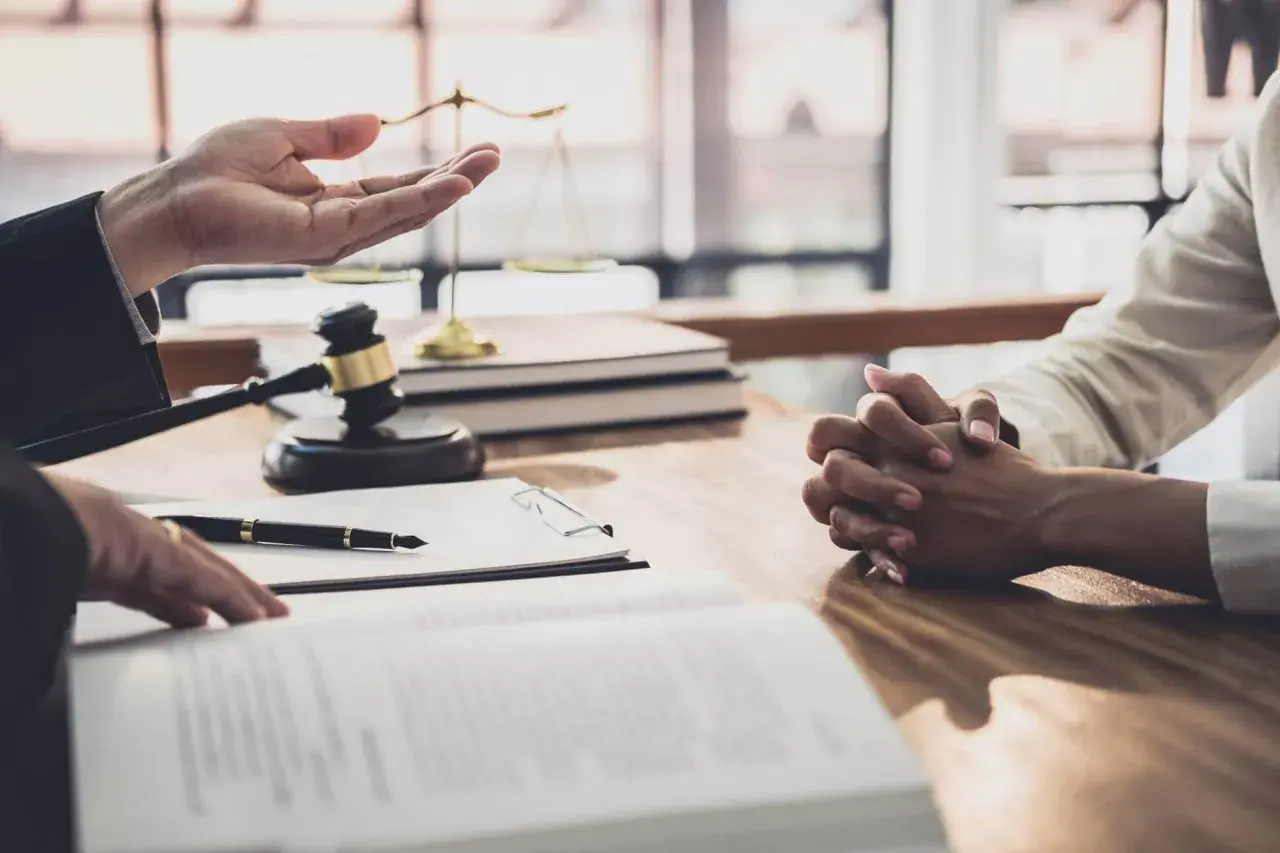 Prawnik omawia z klientem formalności związane z wnioskiem o stwierdzenie nabycia spadku. Na stole leżą dokumenty, młotek sędziowski i waga sprawiedliwości.
