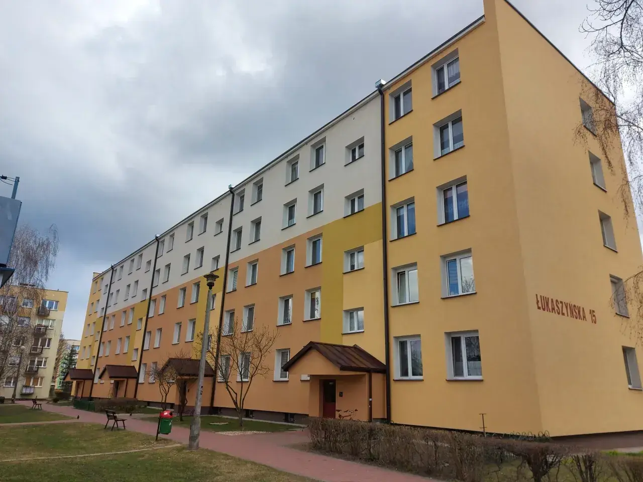 Długi blok mieszkalny przy ul. Łukaszyńskiej 15, pomalowany na żółto i biało. Spółdzielnia mieszkaniowa nie chce naprawić dachu, mimo że przecieka.