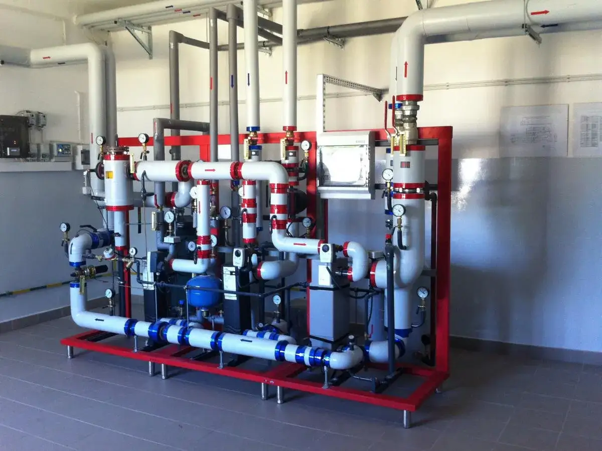Skomplikowana instalacja rurowa z manometrami, zaworami i pompami, stanowiąca element centralnego ogrzewania z sieci miejskiej.
