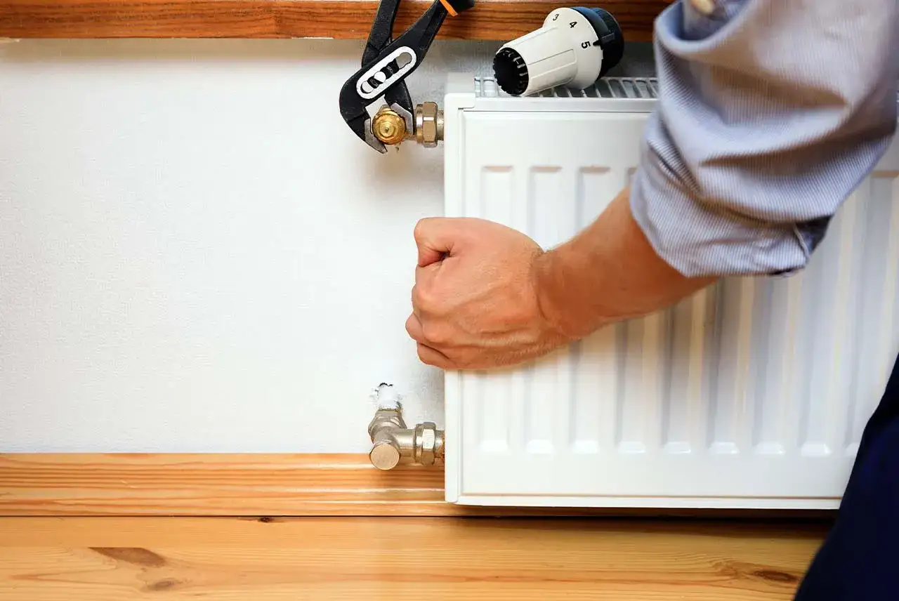 Instalator pokazuje, jak założyć termostat na grzejnik, używając klucza do dokręcenia zaworu.