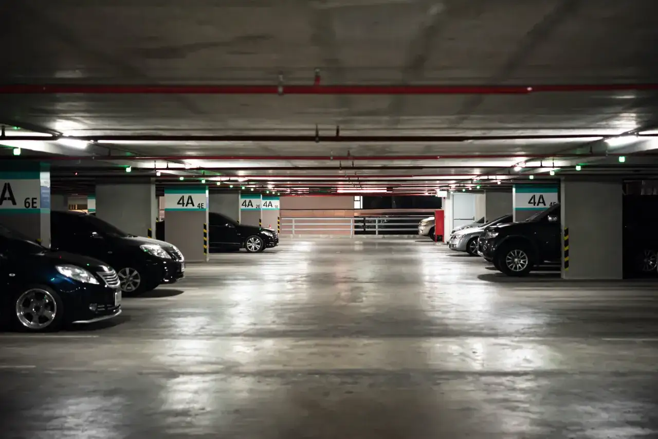 Podziemny parking z rzędami samochodów. Widać numery miejsc, np. 4A, 6E. Może to być miejsce, gdzie naliczane są opłaty za garaż we wspólnocie mieszkaniowej.