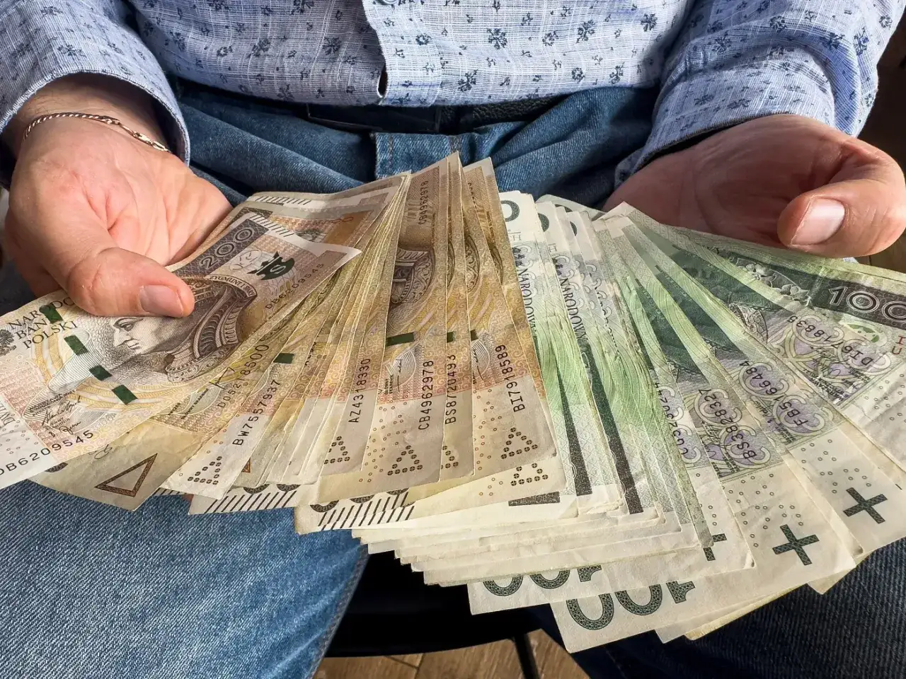 Ręce trzymające stos banknotów, symbolizujących umowę darowizny pieniędzy.